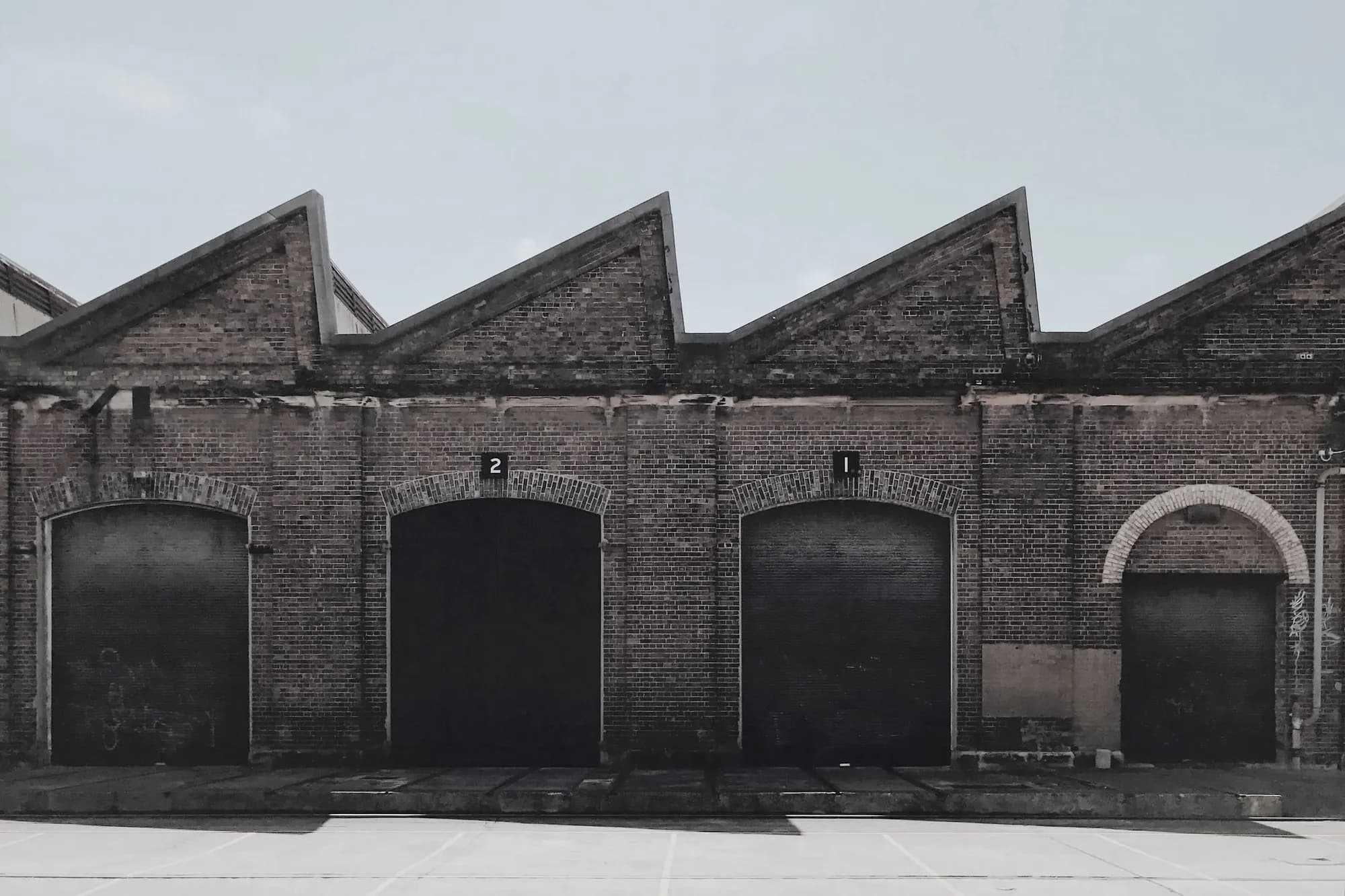 A long brick depot with a saw-tooth roof and four tall arched bay doors