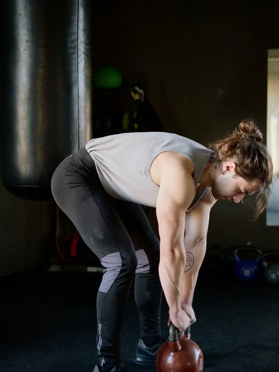 A woman in a dark gym bending to lift a kettlebell from the floor