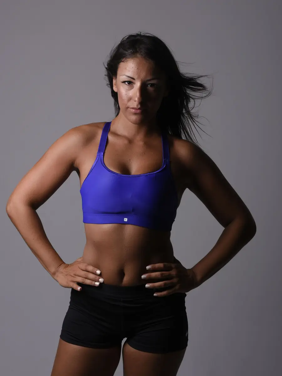 A lifting coach standing with her hands on her hips against a grey studio wall