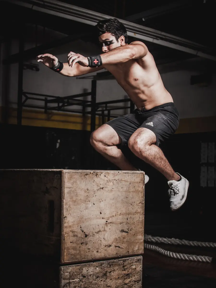 An athlete mid-air in a box jump in a dark training hall