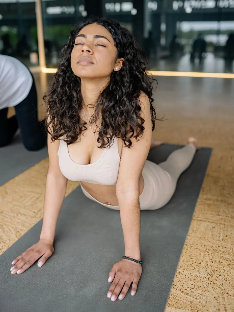 A woman stretching up from a mat in a bright studio, eyes closed