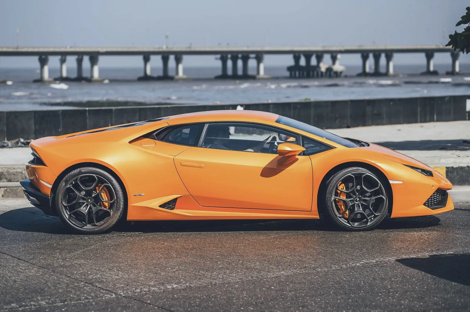An orange supercar parked side-on by the sea