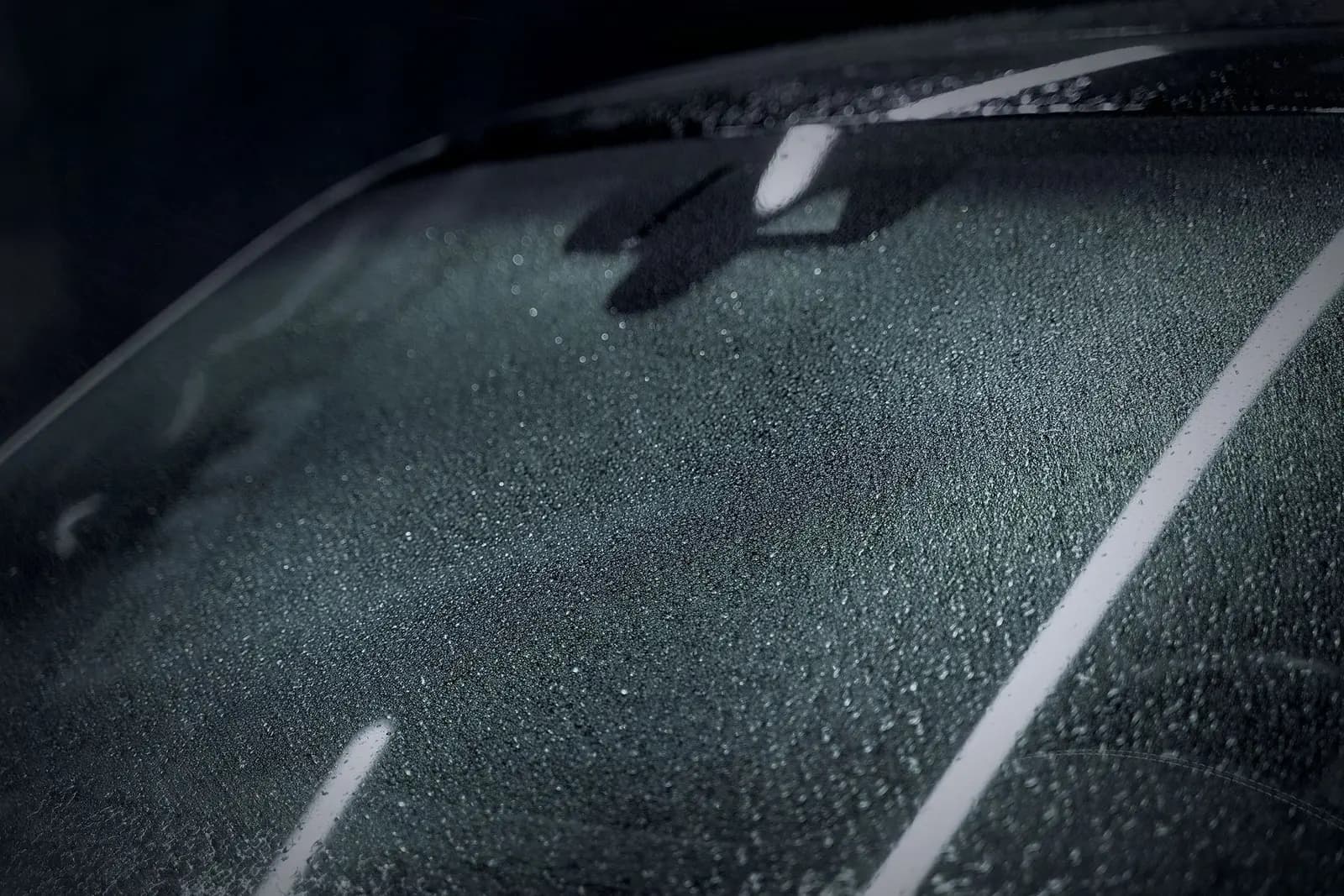 Raindrops beading on the dark windscreen of a car