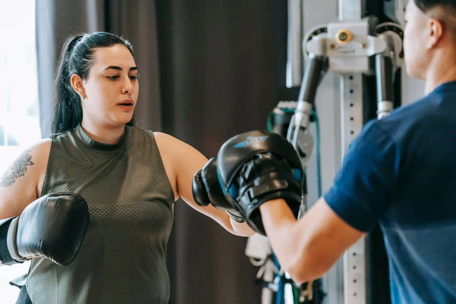 A woman in boxing gloves punching pads held by a coach