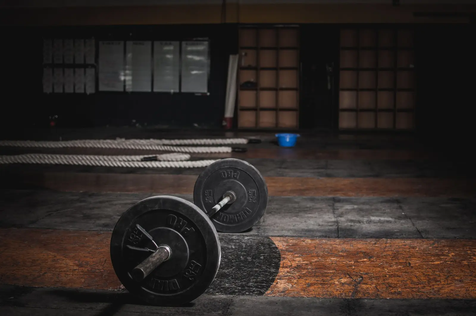 A loaded barbell on the wooden floor of a dim strength room