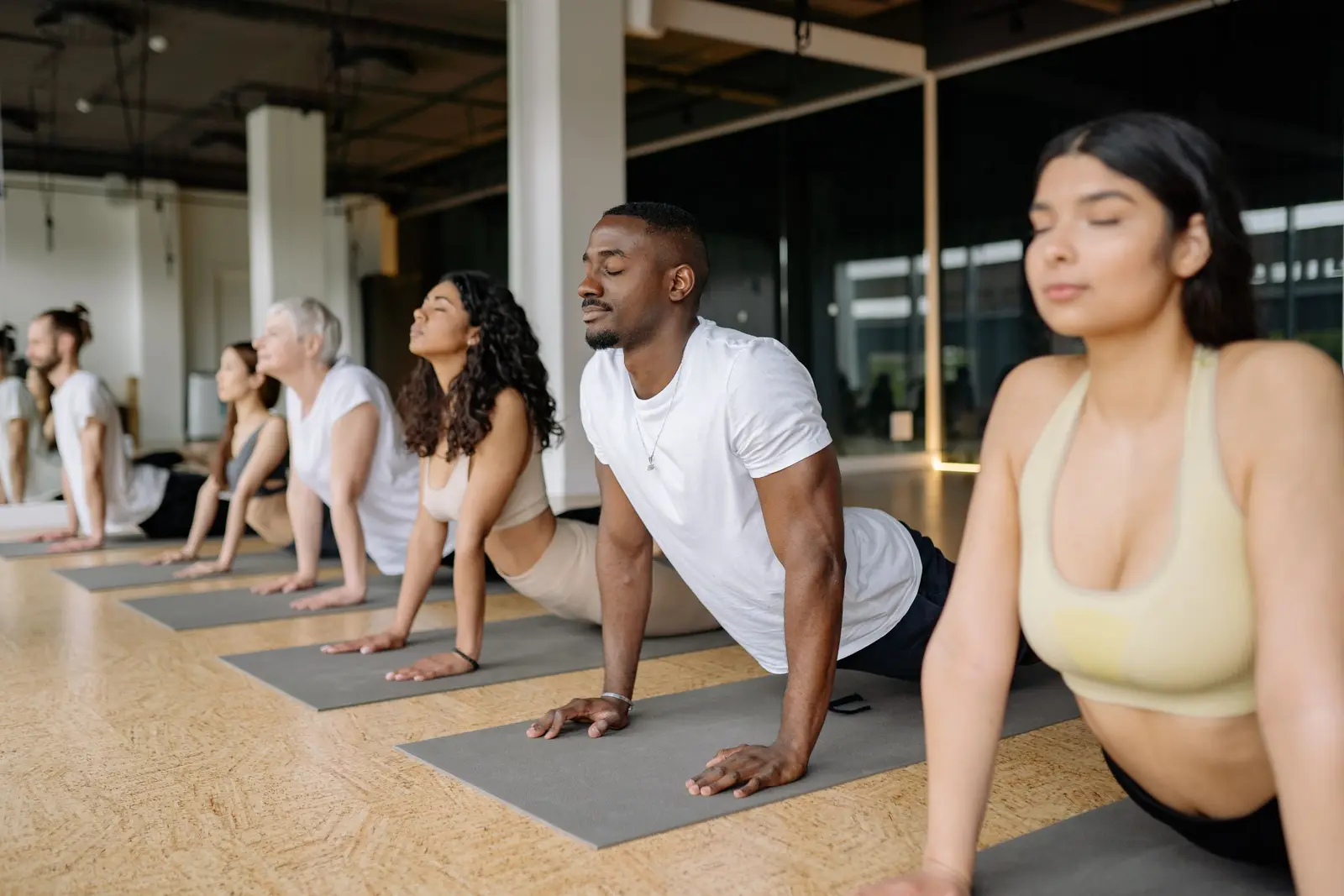 A mixed class in an upward-dog stretch on mats in a bright studio