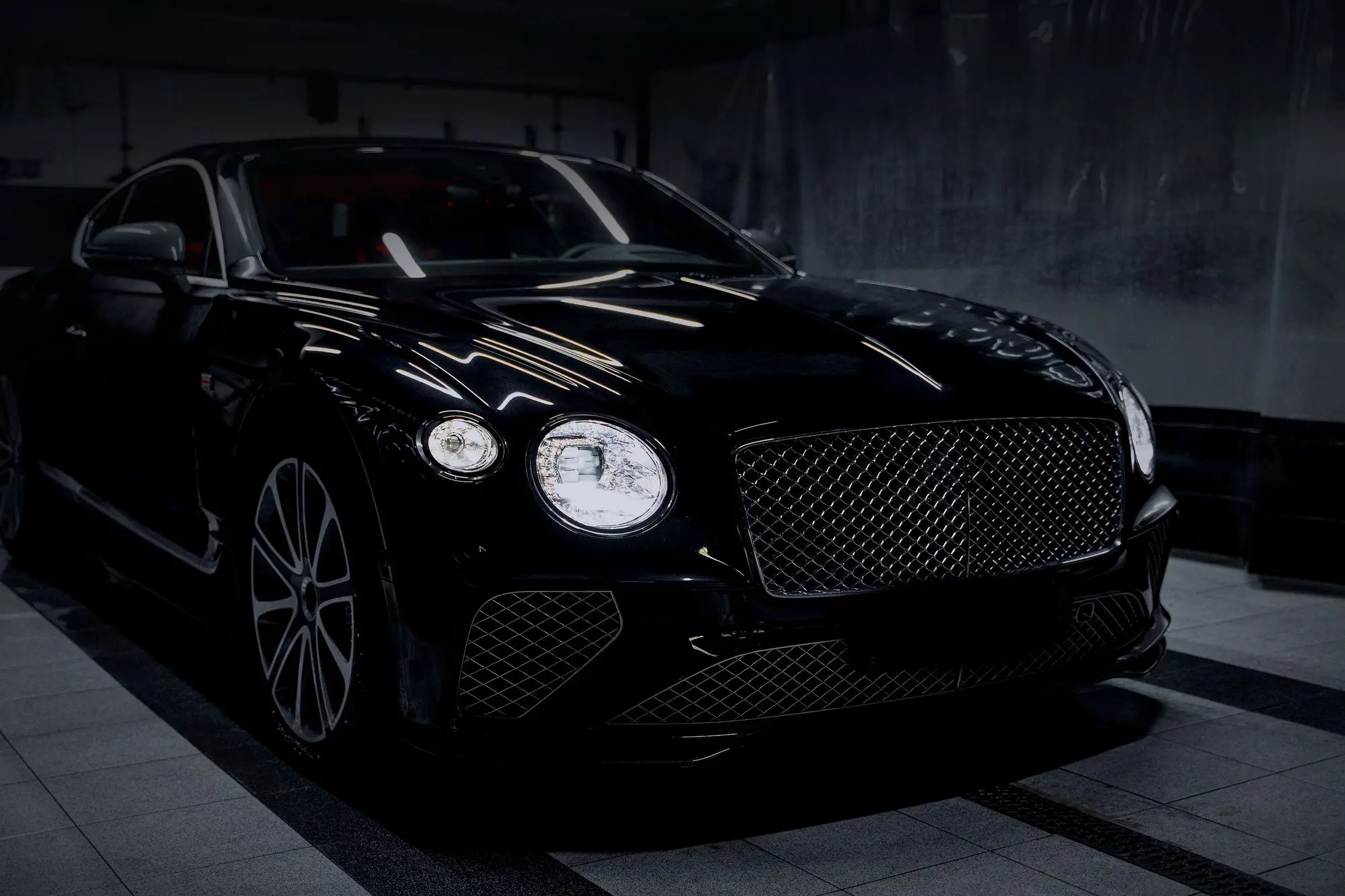 A black grand tourer in a dark studio, seen from the front three-quarter with its round headlamps lit