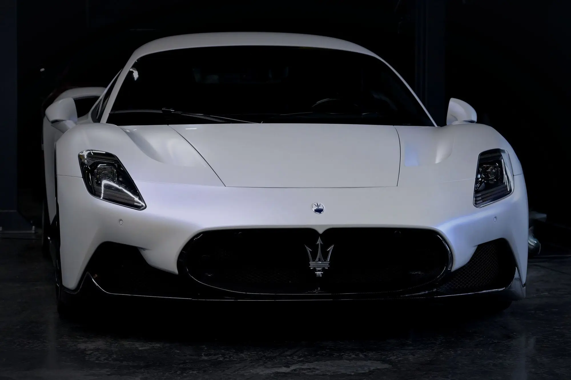 A white mid-engined sports car facing the camera in a dark showroom