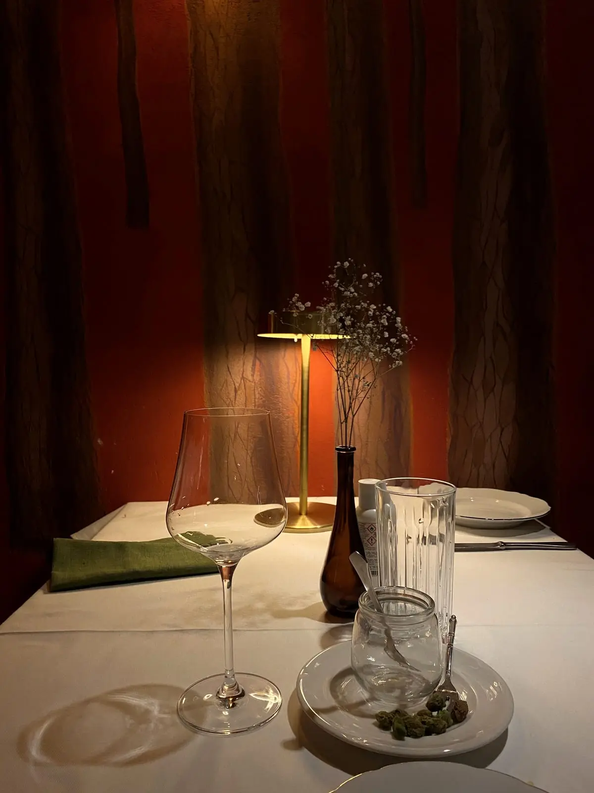 A candle-lit restaurant table set with wine glasses and a small lamp against a deep red wall