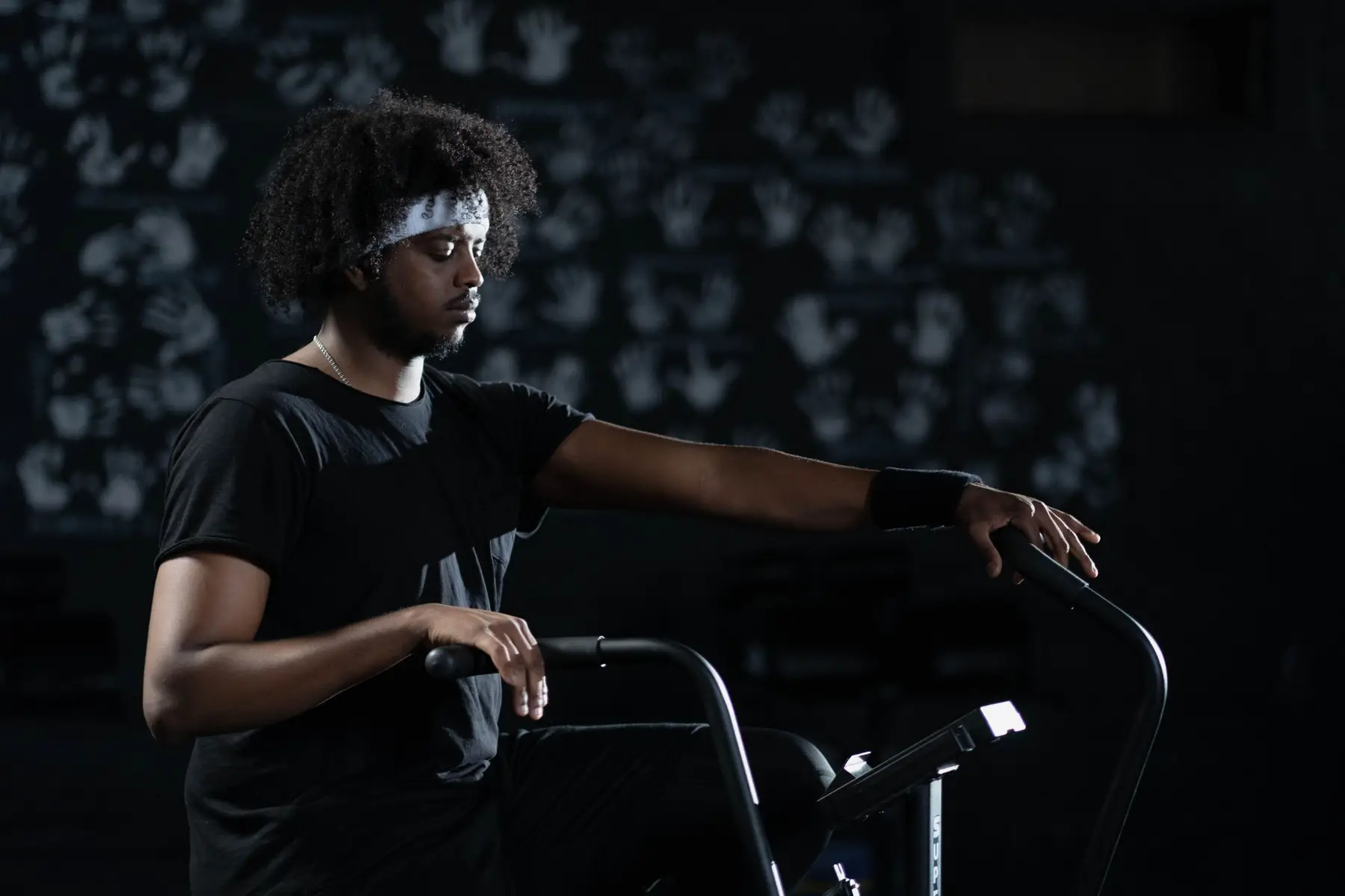 A man in a headband resting his hands on an air bike
