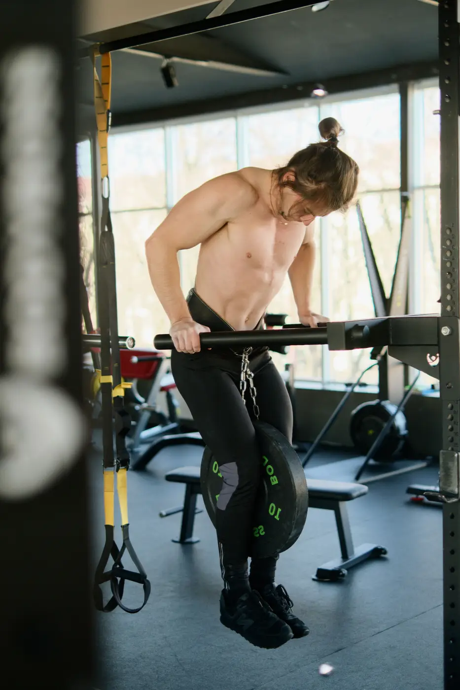 A man gripping a barbell in a rack by a bright window