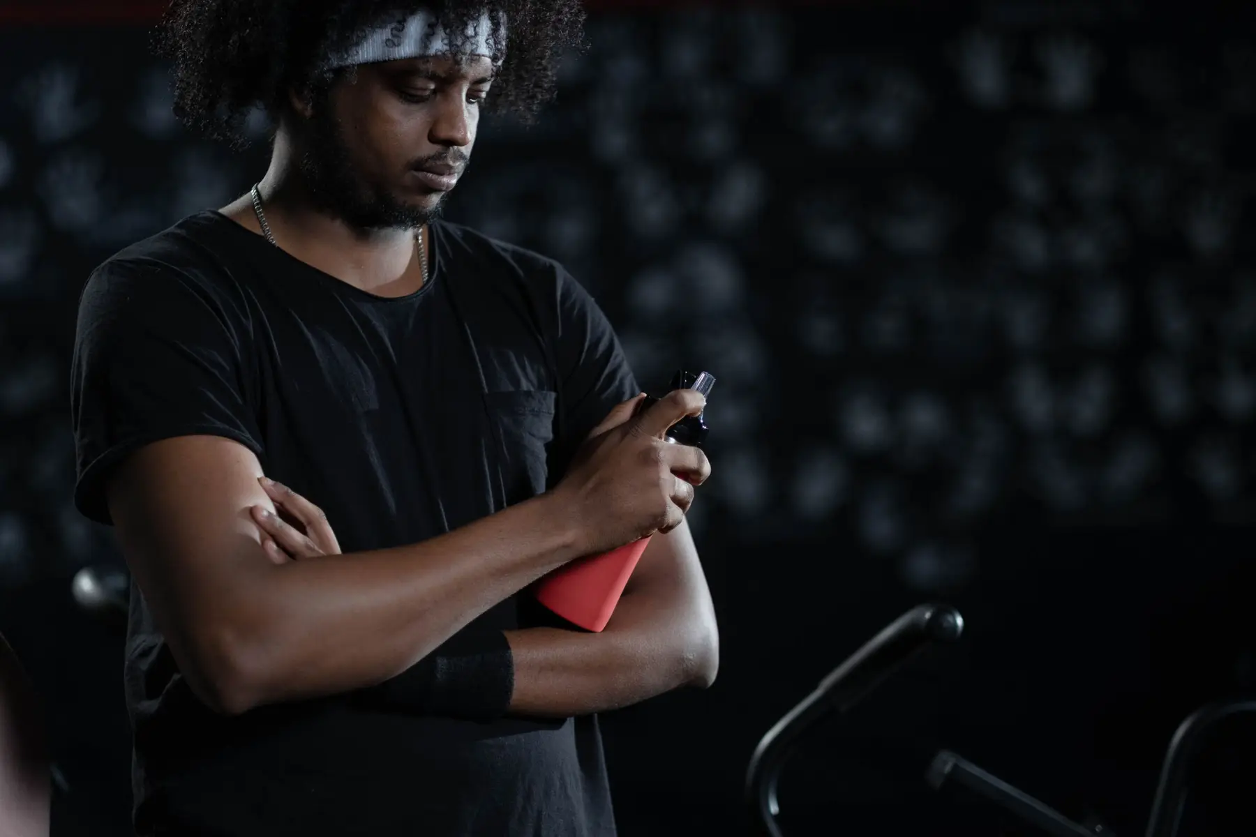 A coach in a black T-shirt checking his phone beside an air bike