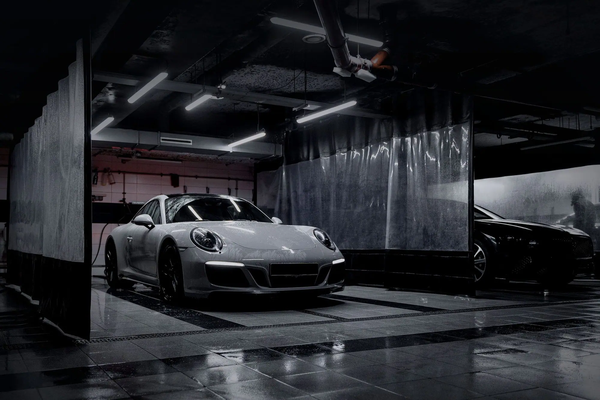 A silver sports coupe parked in a dark showroom garage under strip lights, its floor reflecting the lights