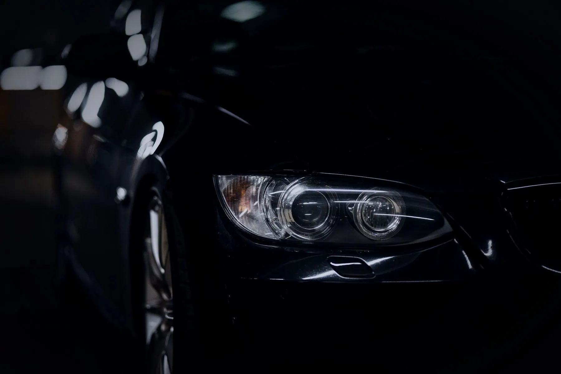 Light catching the headlamp and front wheel arch of a black car in near darkness