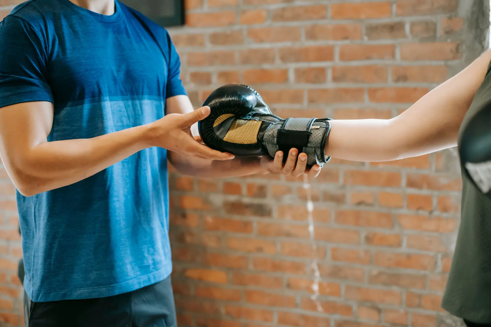 A coach passing a boxing glove to a trainee against a red brick wall